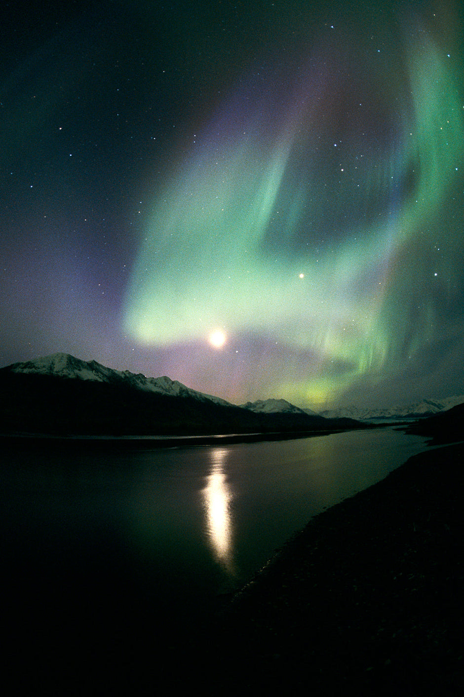 Autumn moon glowing through green aurora borealis curtains in Alaska
